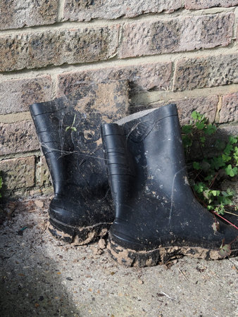 a pair of muddy black wellngton boots near a brick wall