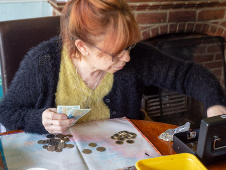 a woman sat at a table counting cash with a cash box nearby