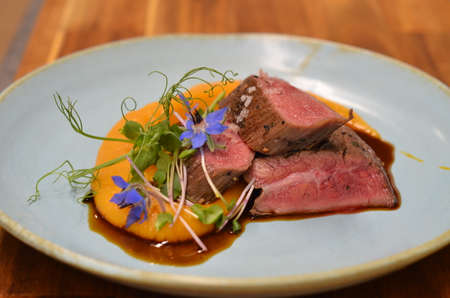roasted flank steak with mashed sweet potatoes and mixed herb green salad served on a blue plateの写真素材