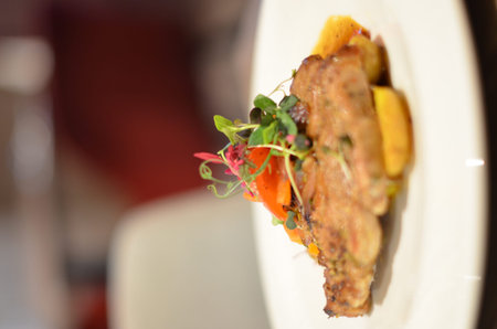 grilled roasted pork neck with red pepper and fresh colored micro herbs on a plate with sauce...