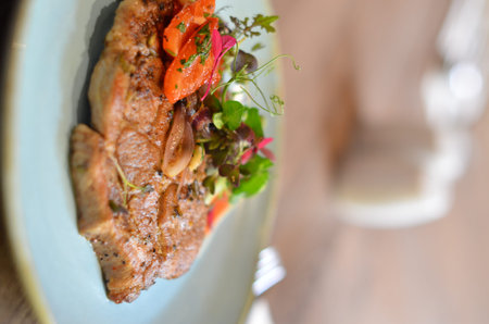grilled roasted pork neck with red pepper and fresh colored micro herbs on a blue plate