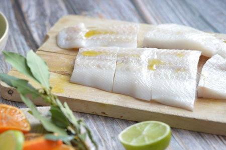 Raw cod fish fillets with lemon and bay leaf on cutting board.の写真素材
