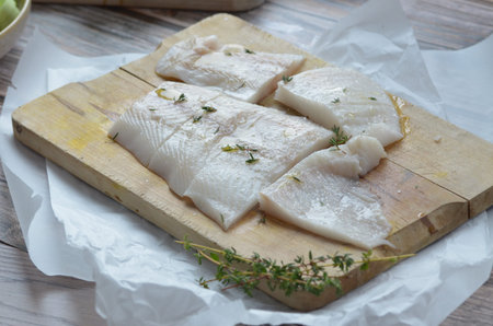 Raw cod fish fillets on wooden cutting board with thyme and lemon