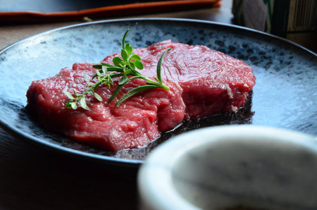 raw beef steak on a plate with rosemary and sauce on a wooden tableの写真素材