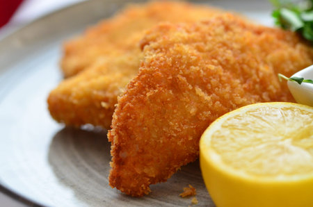 Fried fish in breadcrumbs on a plate with lemon and parsleyの写真素材