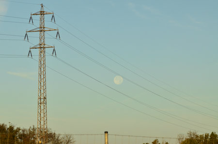 High voltage power line and moon in the blue sky at sunset.の写真素材