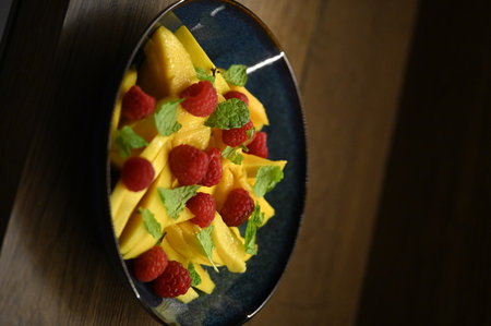 Mango salad with raspberries and mint in a blue plateの写真素材