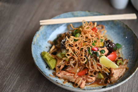 Thai spicy noodle with pork and vegetables on wooden table.