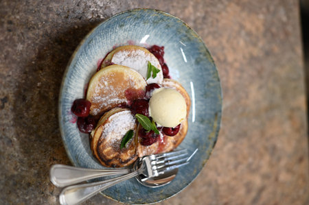 Pancakes with cherry, ice cream and mint on a plate. A beauty plated dessert featuring fluffy golden pancakes dusted with powdered sugar, served with juicy red cherries in syrup.の写真素材
