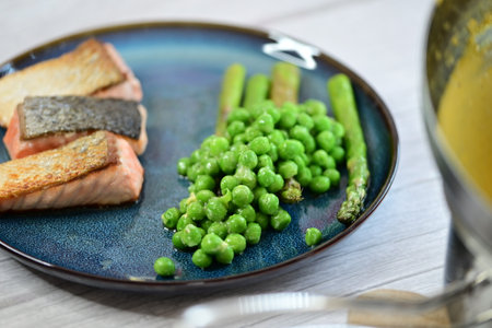 Grilled salmon with green peas on a blue plate on a wooden tableの写真素材