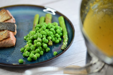 Grilled fish with green peas on a blue plate on a wooden tableの写真素材