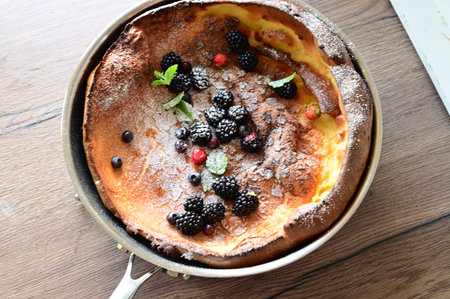 Beautiful close-up of a Dutch Baby pancake breakfast dessert topped with fresh fruit and a dusting...