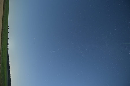 Night sky with stars and milky way over green field in summer