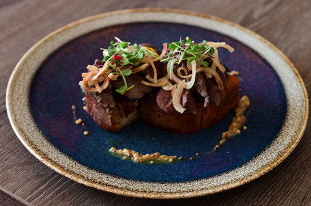 Close-up of toasted bread topped with poultry liver, caramelized onions, and microgreens, served in a European cuisine style with an elegant plated presentation.の写真素材