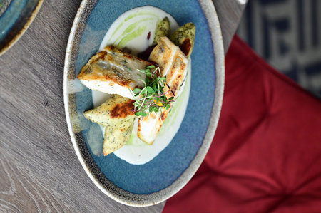 Grilled fish fillet with cream sauce and microgreens on a plate