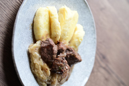 Traditional Czech dish of roasted wild boar with sauerkraut and dumplings, served on a plate in a cozy home-style setting.の写真素材