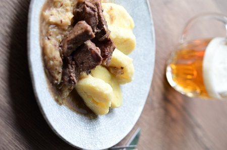 Traditional Czech dish of roasted wild boar with sauerkraut and dumplings, served on a plate in a cozy home-style setting.の写真素材