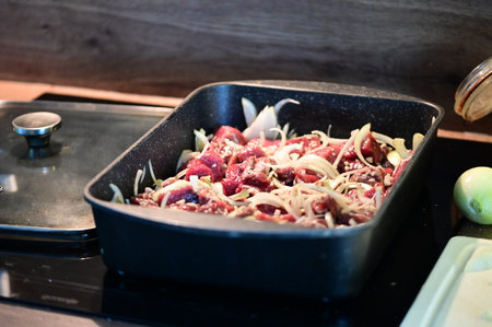 Raw meat with vegetables in a frying pan on a kitchen stove.の写真素材