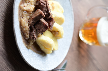 Traditional Czech dish of roasted wild boar with sauerkraut and dumplings, served on a plate in a cozy home-style setting.の写真素材