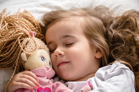 a little girl falls asleep in bed with soft doll, white bedの写真素材