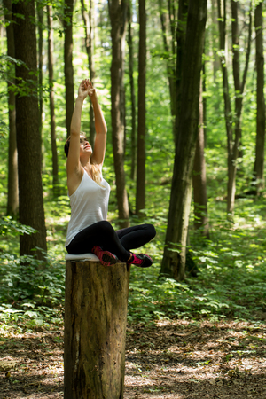 Warming-up. Beautiful sporty girl in the woods on a stump in yoga, sportsの写真素材