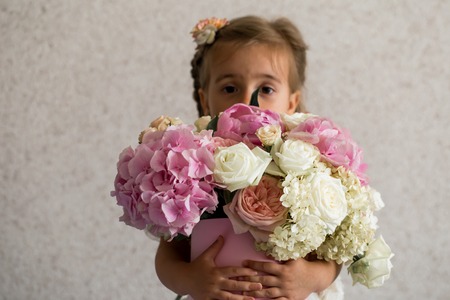 little girl with a big bouquet of fresh flowers, the emotions of a little girl, a girl in a white Board on a light backgroundの写真素材