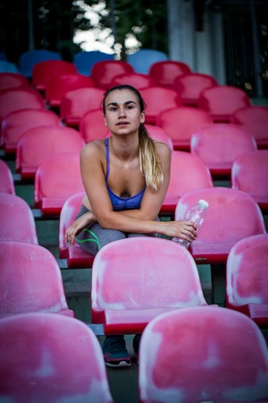 beautiful sporty girl drinking water after running in the stadium, close-up, young sporty womanの写真素材