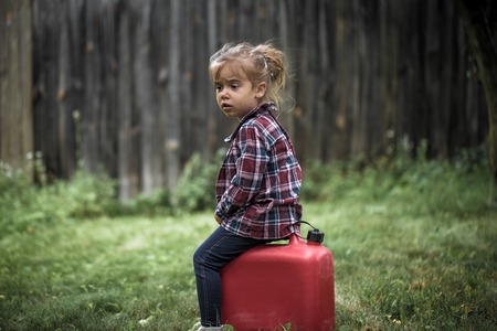 little girl sitting on a red canister, a beautiful background, a sad emotion girlの写真素材