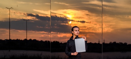 beautiful business girl with white piece of paper on a beautiful mirror background, sunset, purposeful girlの写真素材