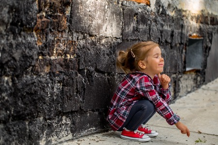 llittle beautiful girl near brick wall with red sneakers and a plaid shirt, emotion girlの写真素材