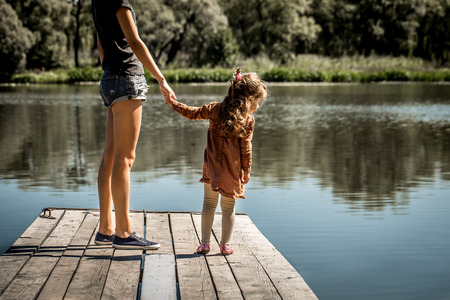 the daughter of a mother hold the hand on the pier at the lakeの写真素材