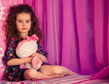little girl playing with soft toys near the window in a baby pink roomの写真素材