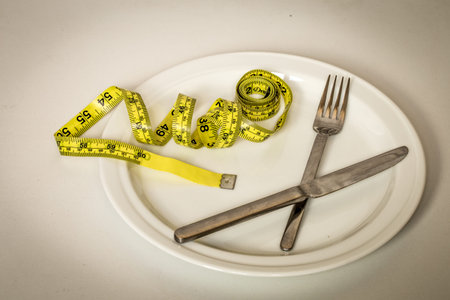 A white plate with a bun, a yellow tape measure and Cutlery on white background,healthy lifestyle,...