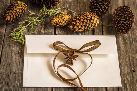 White envelope on wooden background with pine cones and Christmas gift ribbon