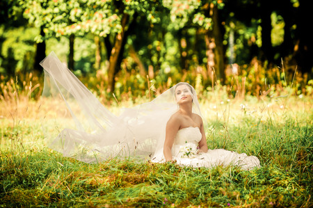 beautiful young bride sitting on a green glade in a beautiful forestの写真素材