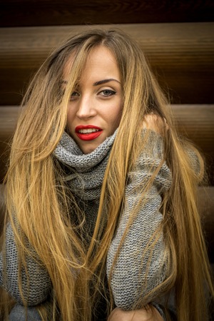 Beautiful girl in a sweater with long hair and red lips is on the background of wooden logsの写真素材
