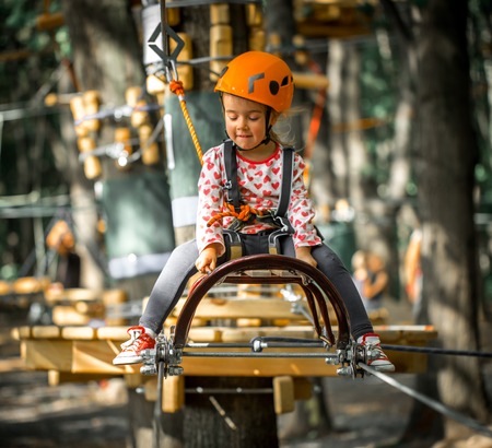 sports happy kid climbs through the ropes, the beautiful girl in the outfit climbing fun in the forest on ropes and different obstaclesの写真素材