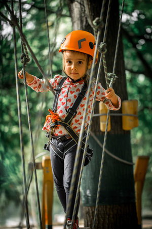 sports happy kid climbs through the ropes, the beautiful girl in the outfit climbing fun in the forest on ropes and different obstaclesの写真素材