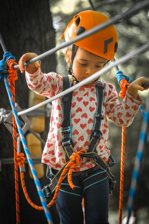 sports happy kid climbs through the ropes, the beautiful girl in the outfit climbing fun in the forest on ropes and different obstaclesの写真素材