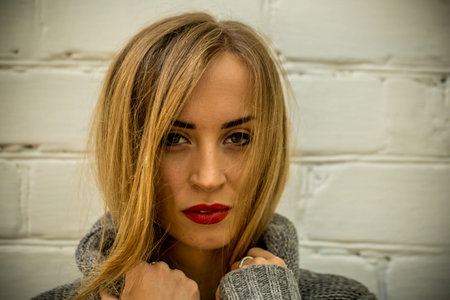 beautiful girl in a sweater with long hair and red lips against the white wallの写真素材