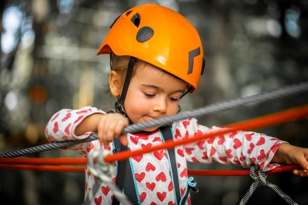 sports happy kid climbs through the ropes, the beautiful girl in the outfit climbing fun in the forest on ropes and different obstaclesの写真素材