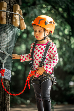 sports happy kid climbs through the ropes, the beautiful girl in the outfit climbing fun in the forest on ropes and different obstaclesの写真素材