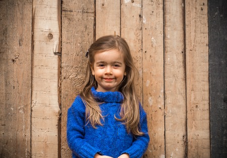 little girl in stylish clothes and a beautiful wooden background, the emotions of a childの写真素材