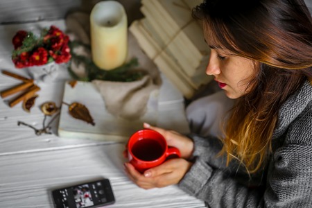 Warm and cozy,and warm concept Beautiful girl with a Cup of tea sitting at white wooden table with book and candleの写真素材