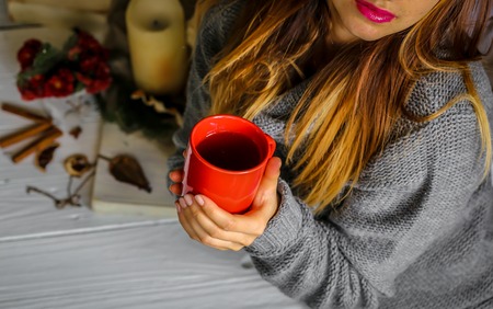 Warm and cozy,and warm concept Beautiful girl with a Cup of tea sitting at white wooden table with book and candleの写真素材