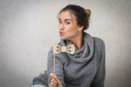 Beautiful young girl with a wooden moustache on a stick,dressed in a cozy knitted sweater