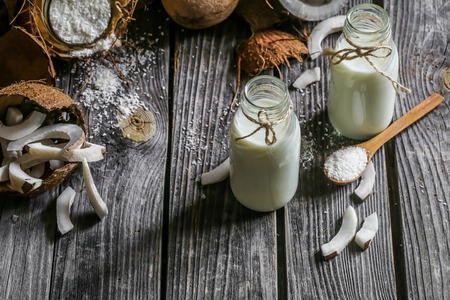Fresh coconuts broken on wooden background with coconut milk in small glass jarsの写真素材