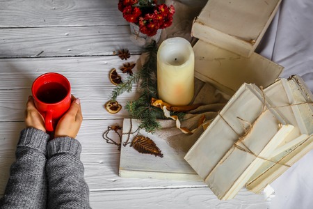 Warm and cozy,and warm concept girl hands with a Cup of tea over white wooden table with book and candleの写真素材