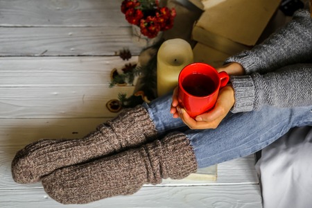 Warm and cozy,and warm concept girls feet in warm knitted socks with a Cup of tea over white wooden table with book and candleの写真素材