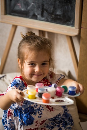 a little girl with colours in hands on the background of the easelの写真素材